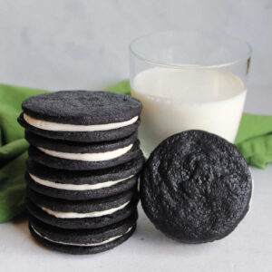Stack of large homemade Oreos next to a glass of milk, ready to eat.