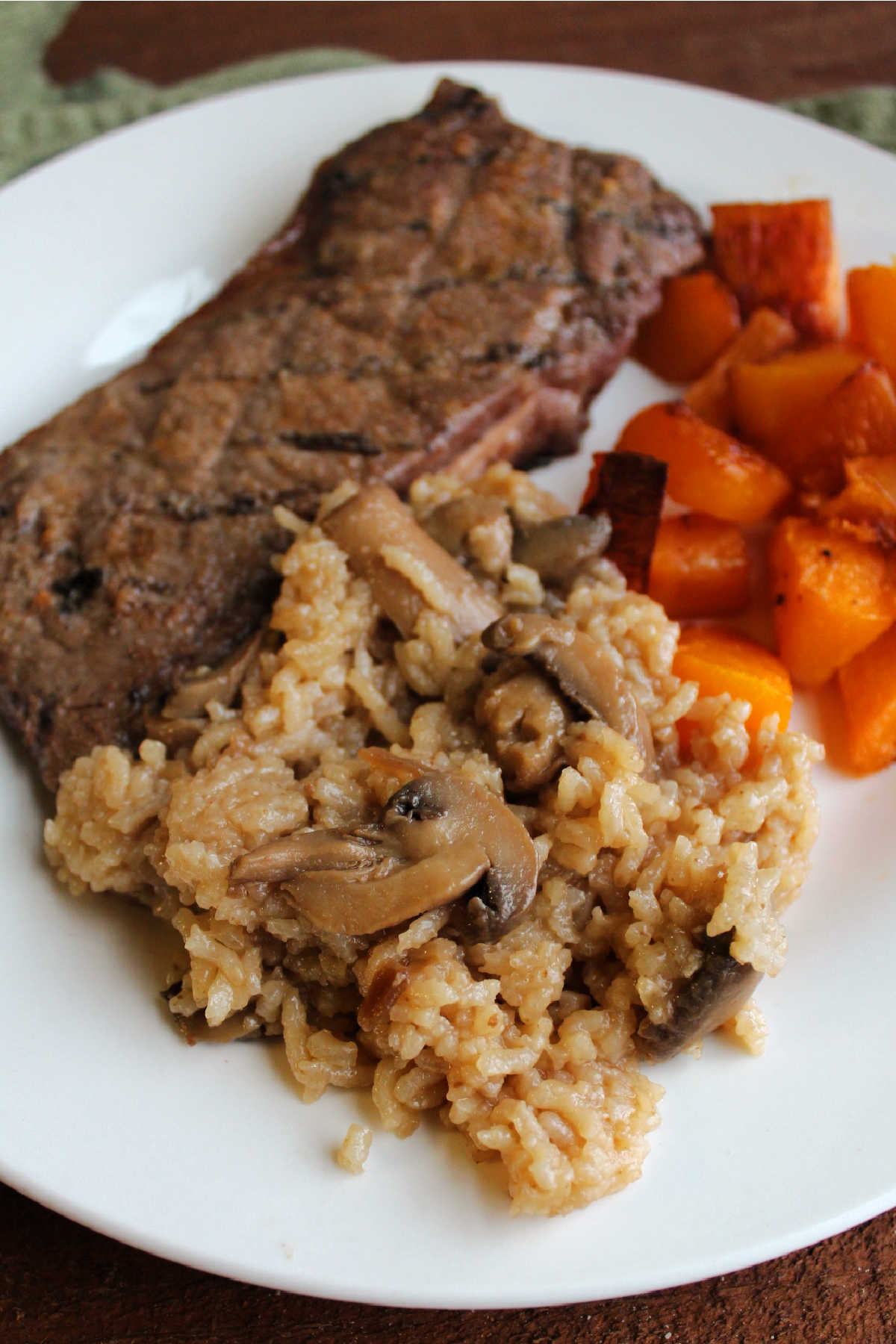 Mushroom baked rice served on dinner plate with steak and roasted butternut squash.