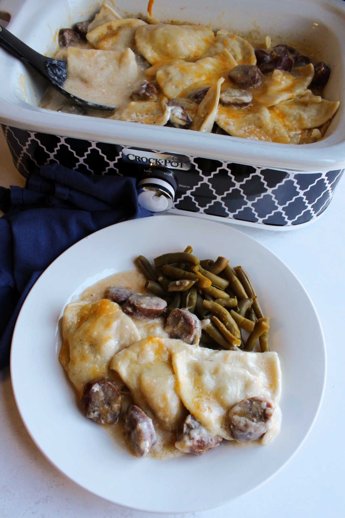 Plate of creamy pierogis and smoked sausage casserole with green beans by slow cooker with remaining pierogi. 