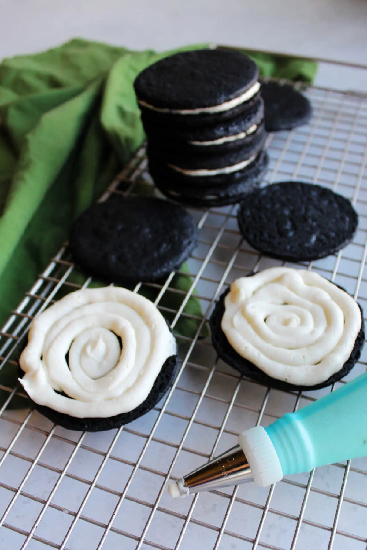 Piping white cream filling onto dark chocolate wafer cookies to make homemade Oreo cookies. 