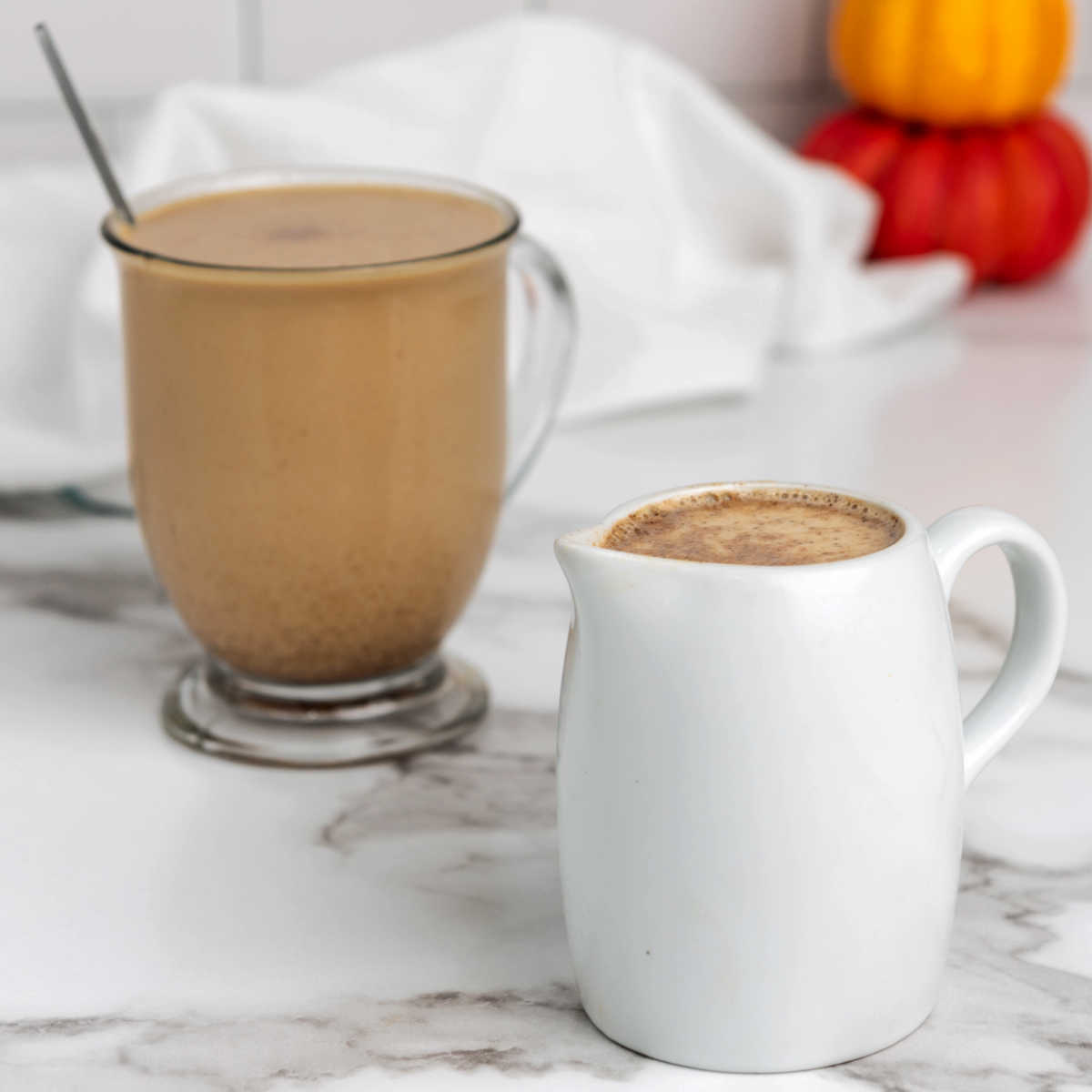 Mug of coffee with pumpkin spice creamer in it next to a small pitcher with additional creamer.
