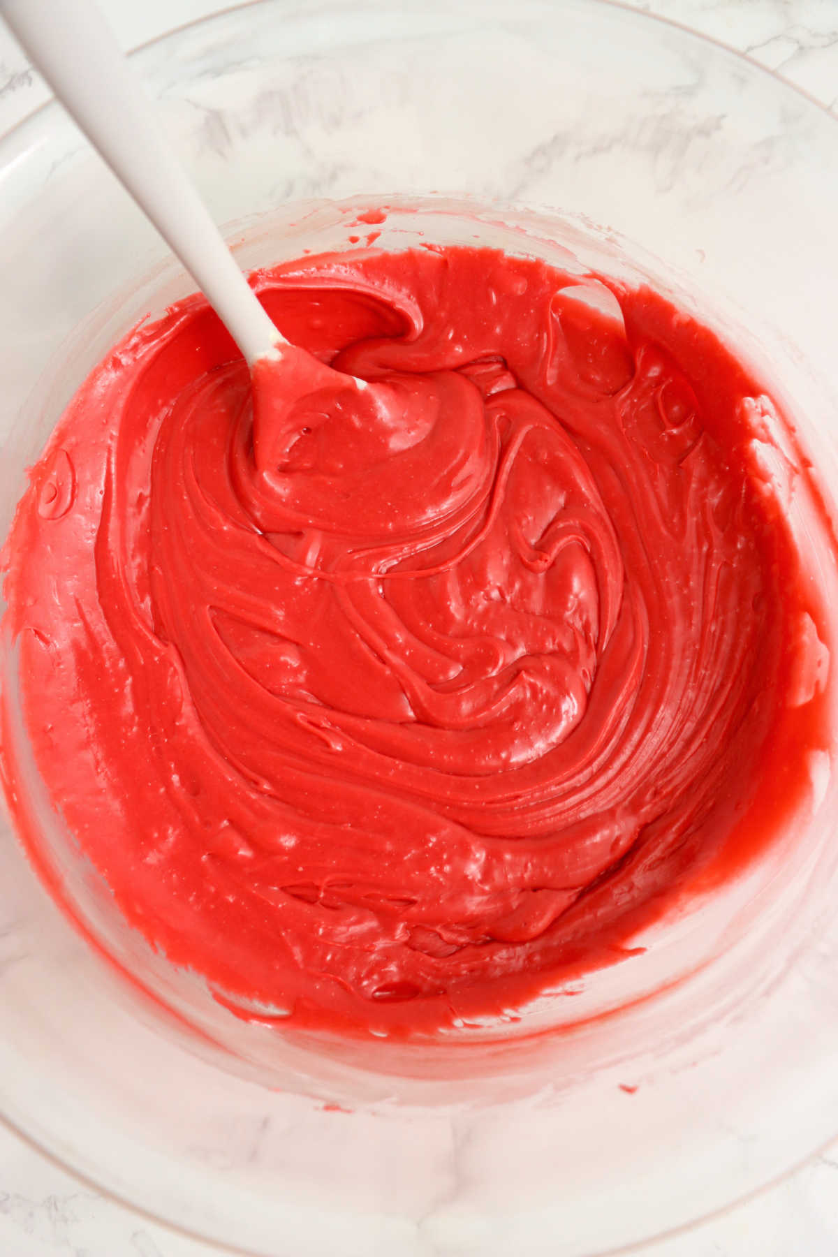 Red velvet cake mix stirred into melted chocolate making a smooth bright red mixture.