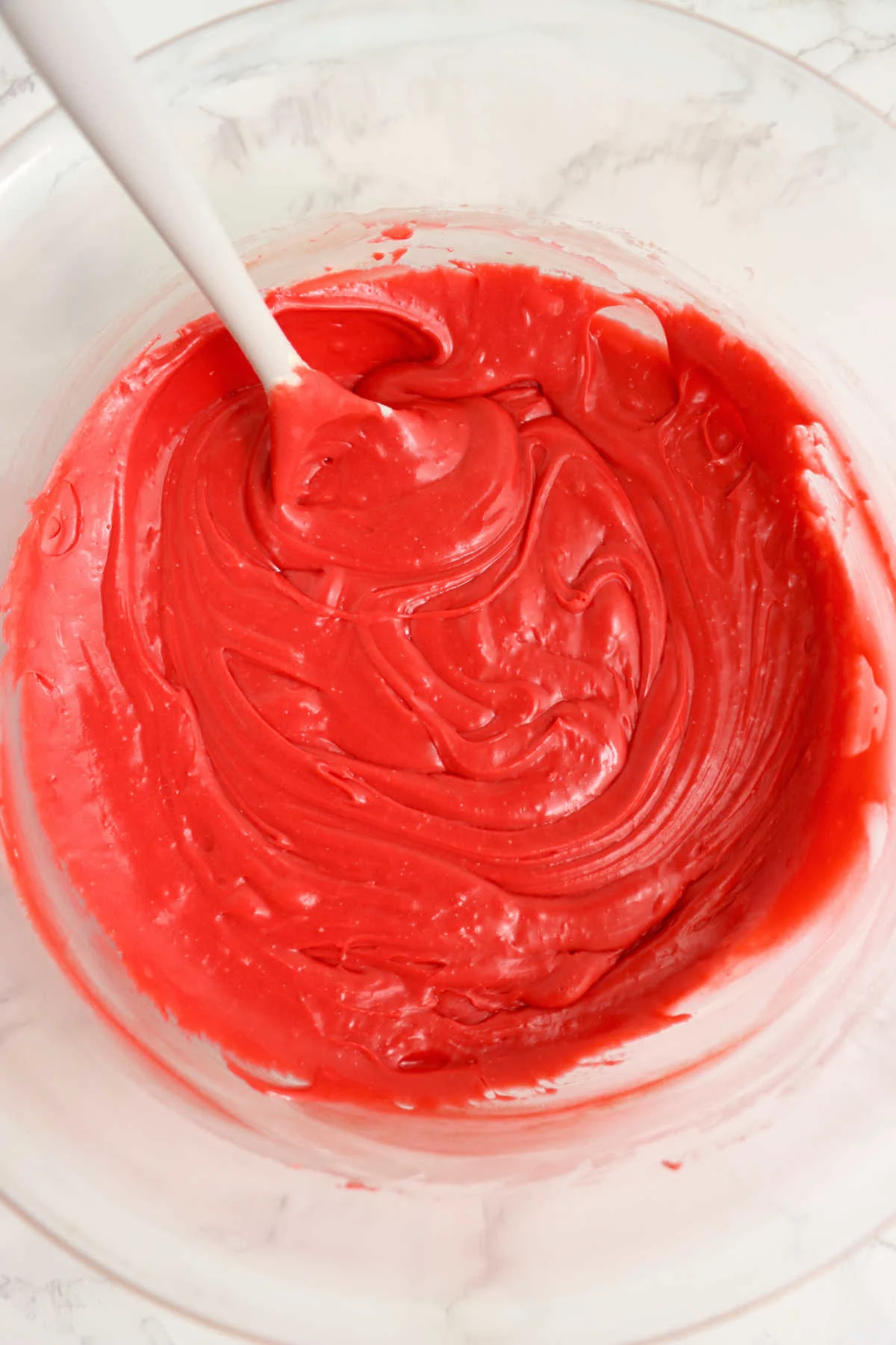 Red velvet cake mix stirred into melted chocolate making a smooth bright red mixture.