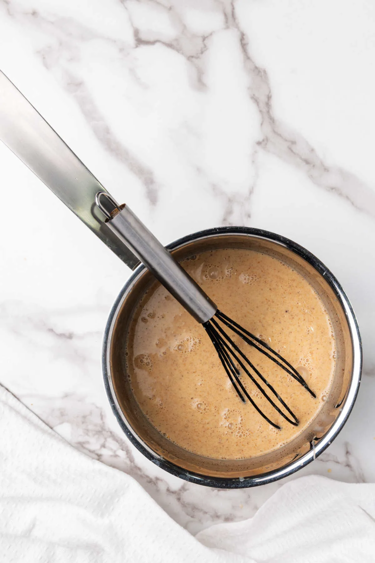 Saucepan of pumpkin spice coffee creamer with whisk.