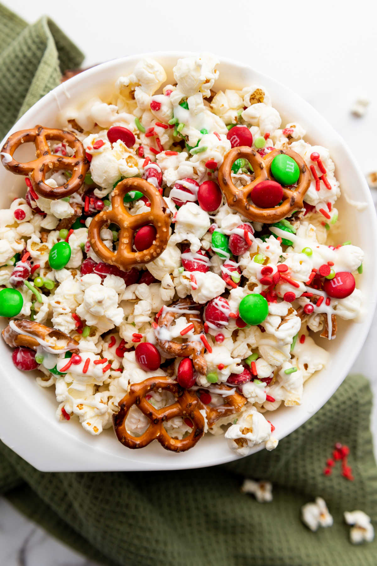 Looking down on bowl of popcorn with white chocolate, pretzels, and red and green candies. 