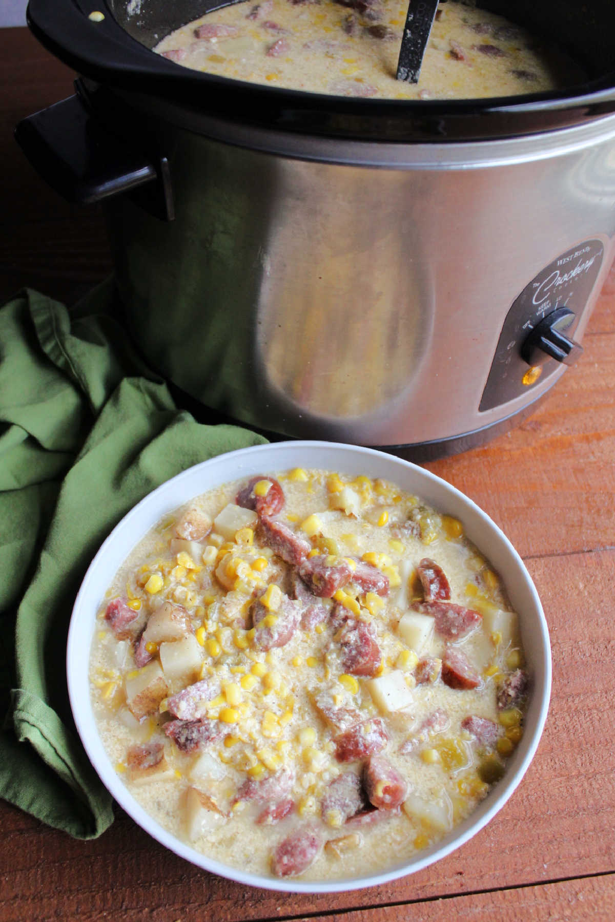 Bowl of creamy smoked sausage chowder served next to slow cooker it was cooked in. 