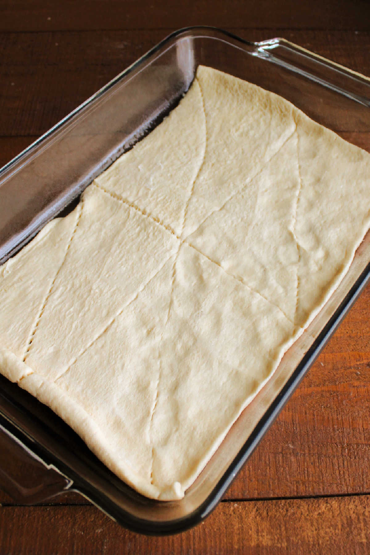 Sealing the seems on crescent dough and pressing it into a 9x13-inch pan.