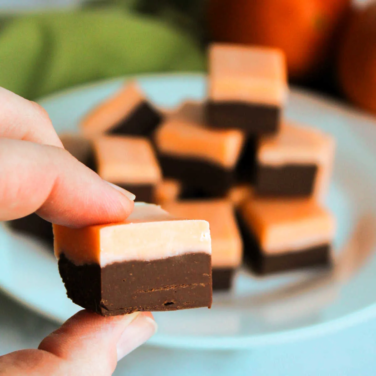 Hand holding piece of fudge with a chocolate layer on the bottom and a layer of creamy orange fudge on the top.