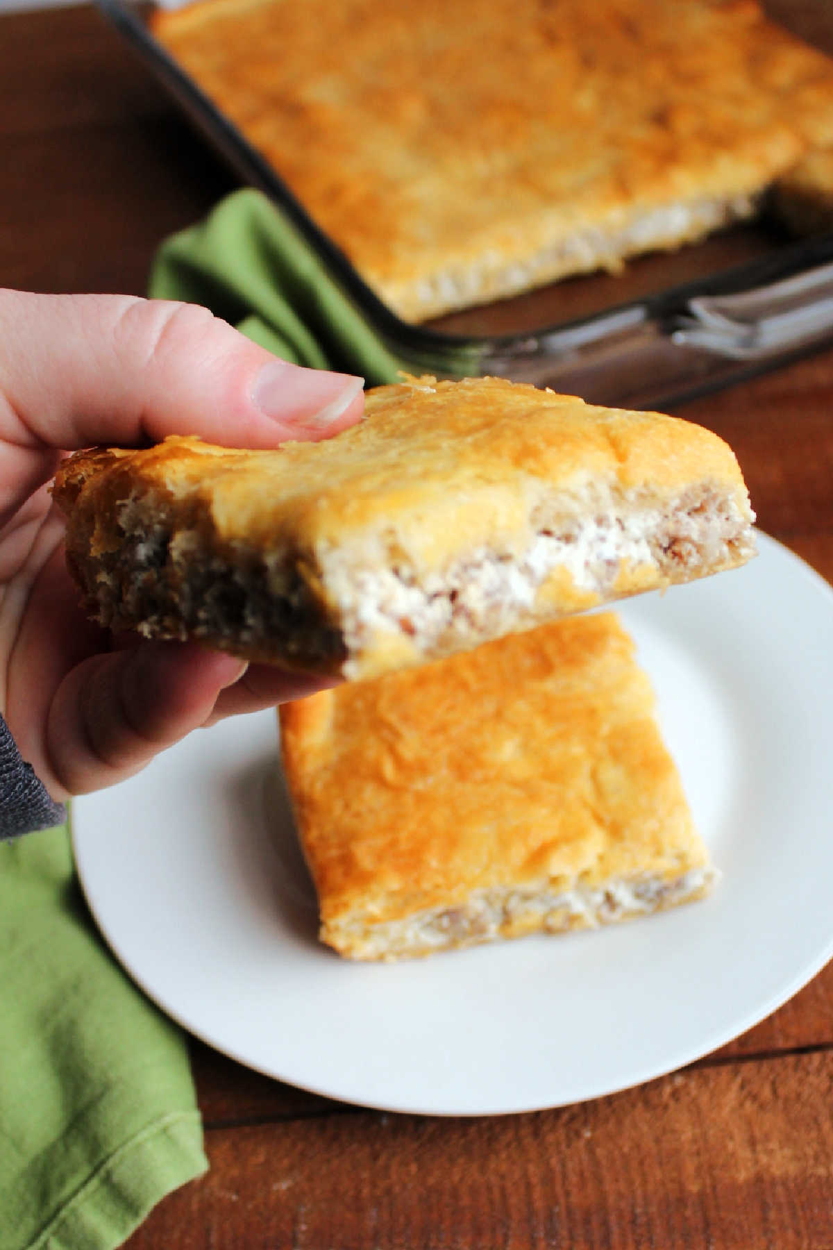 Hand holding cream cheese and sausage crescent bar showing cheesy sausage filling.