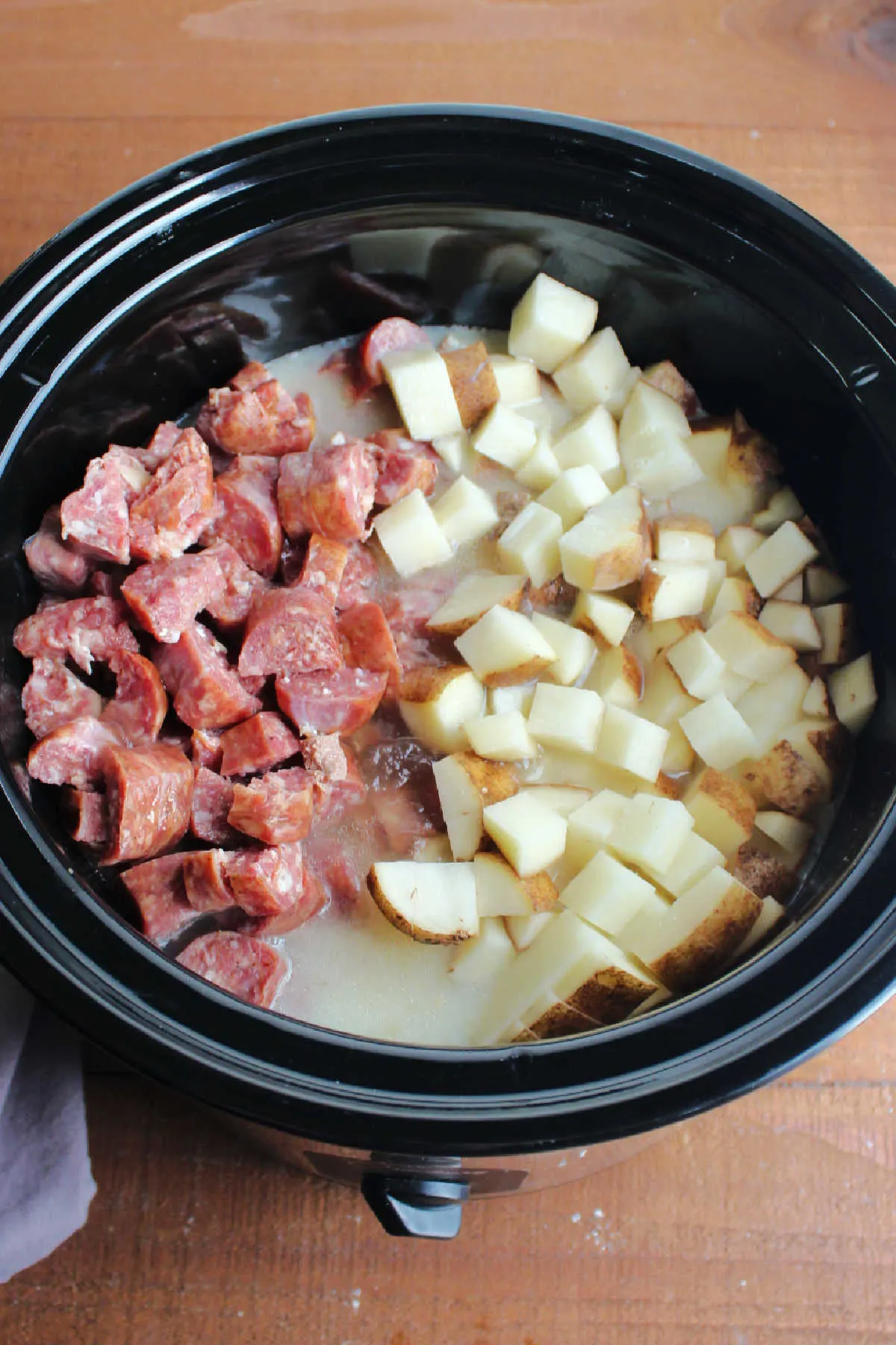 Smoked sausage, diced potatoes, stock and evaporated milk added to crockpot ready to cook.
