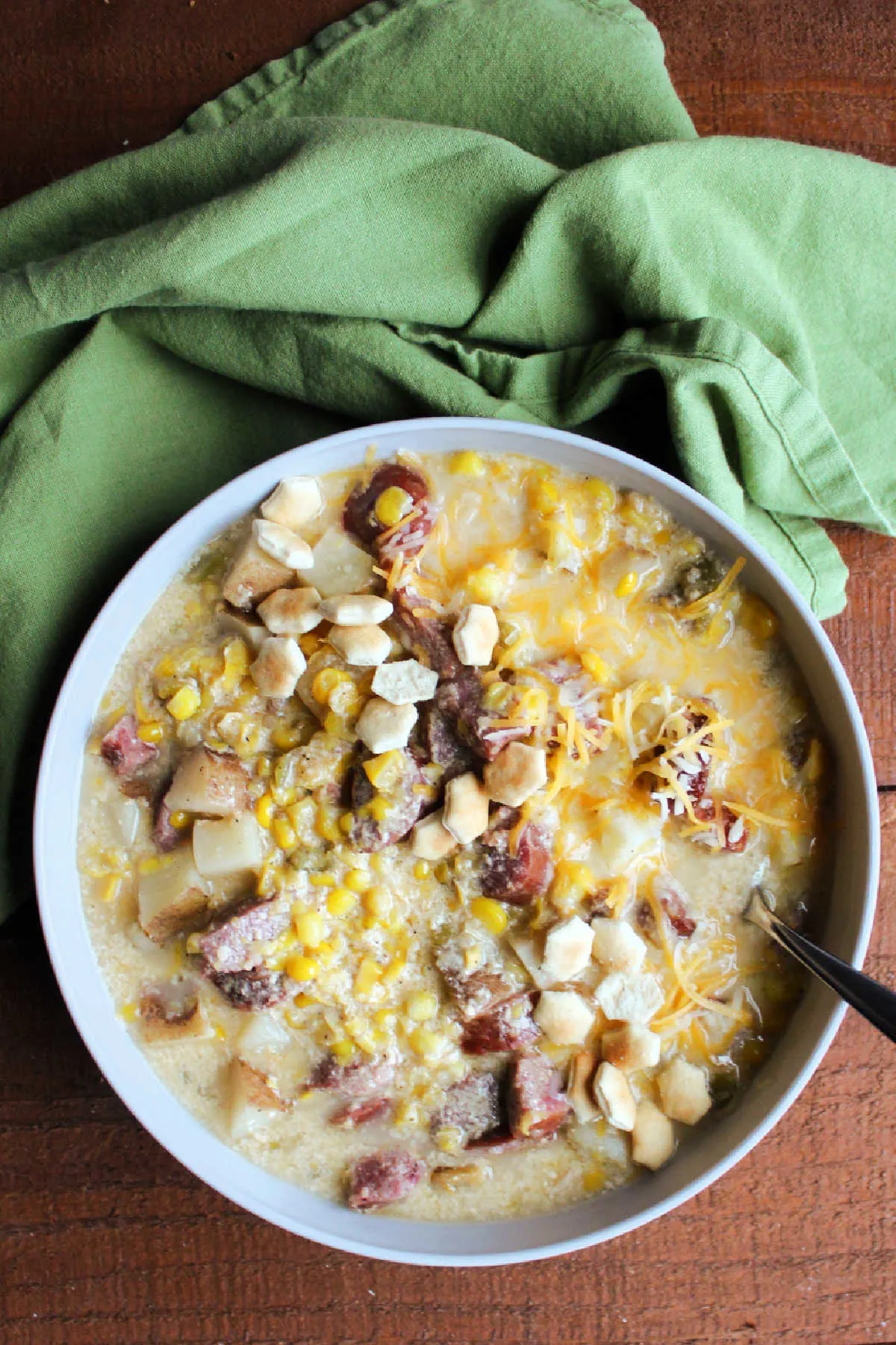 Bowl of kielbasa chowder served with shredded cheese and oyster crackers.