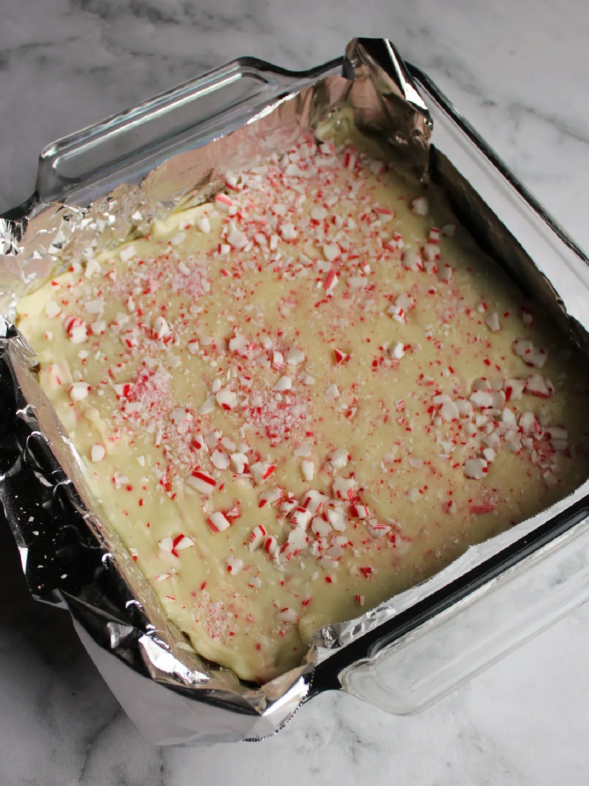 Pan of fudge with white chocolate layer and bits of candy cane pressed into the top. 