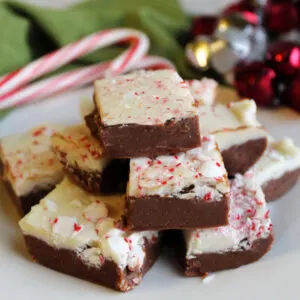 Stack of peppermint bark fudge with chocolate bottom layer, white chocolate top layer and bits of crushed candy cane on top.