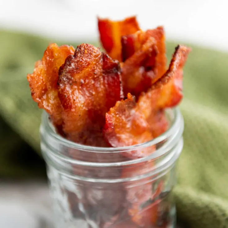 Close up of strips of maple candied bacon with maple syrup and brown sugar coating standing up in jar.