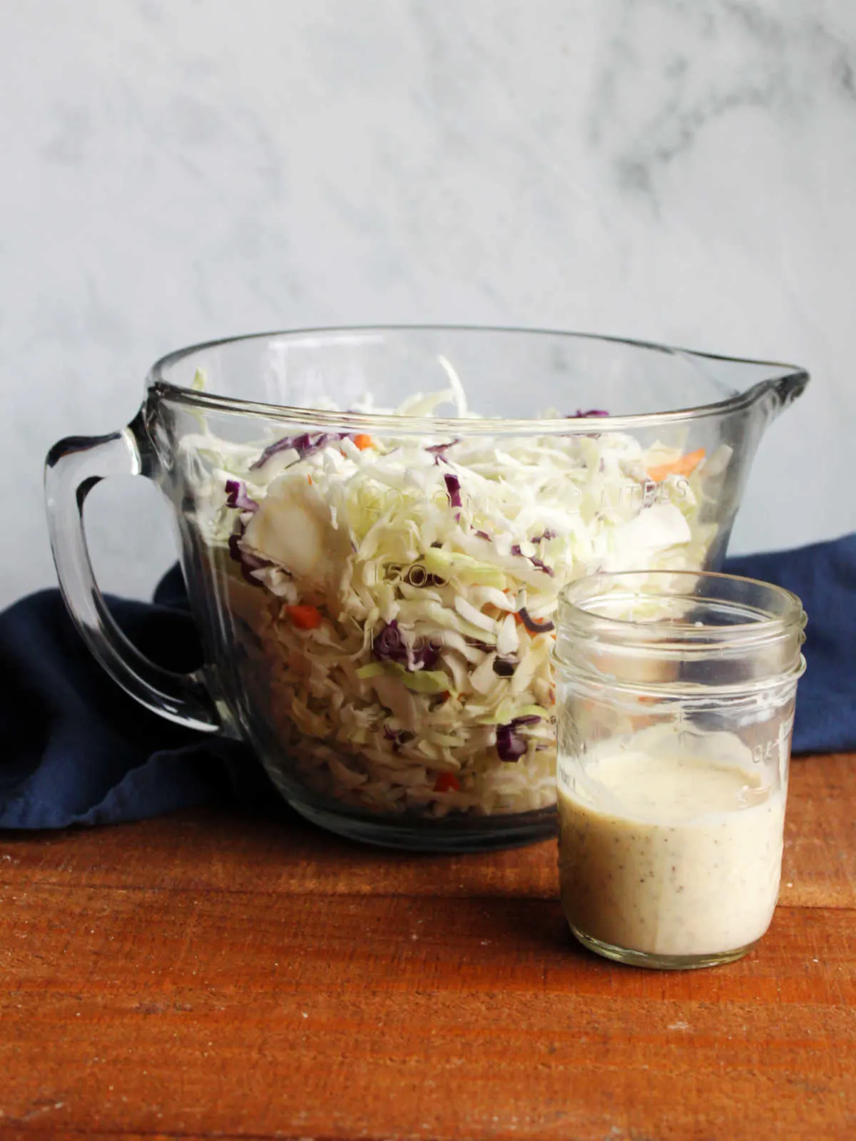 Large glass bowl filled with shredded cabbage next to jar of condensed milk dressing.