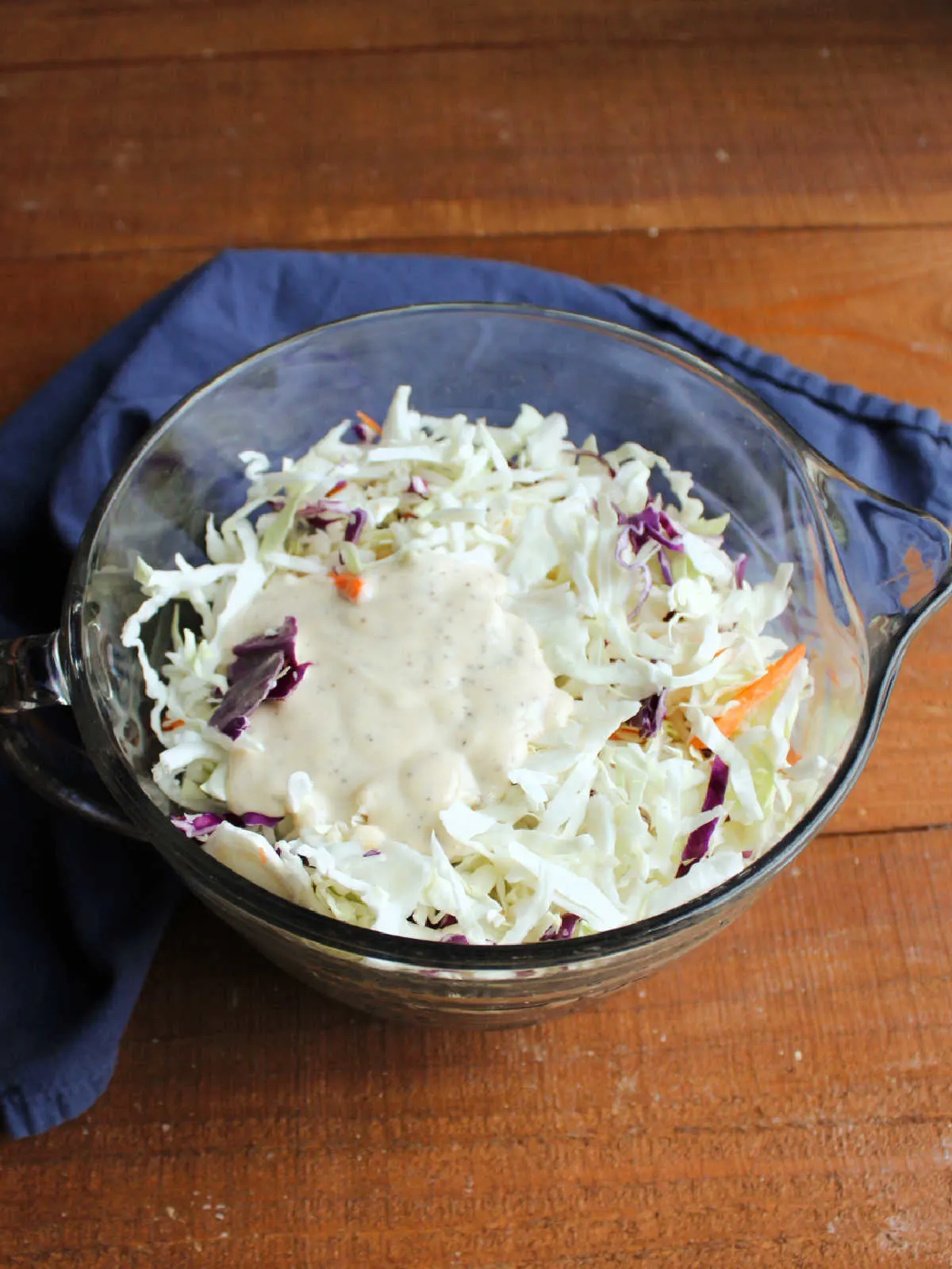 Small pool of creamy dressing on top of shredded cabbage in a glass bowl.
