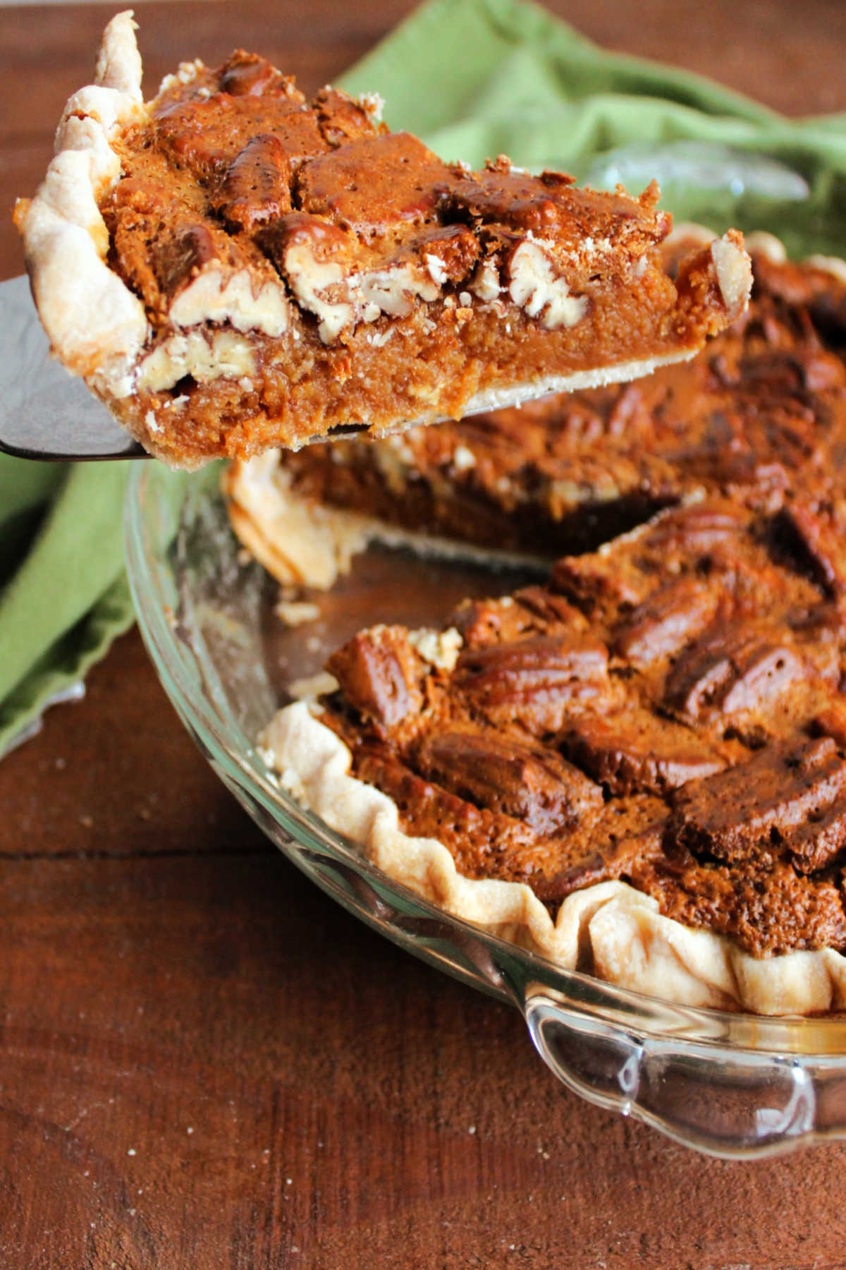 Lifting a slice of caramel pecan pie out of the pan showing the layer of pecans and the caramel filling.