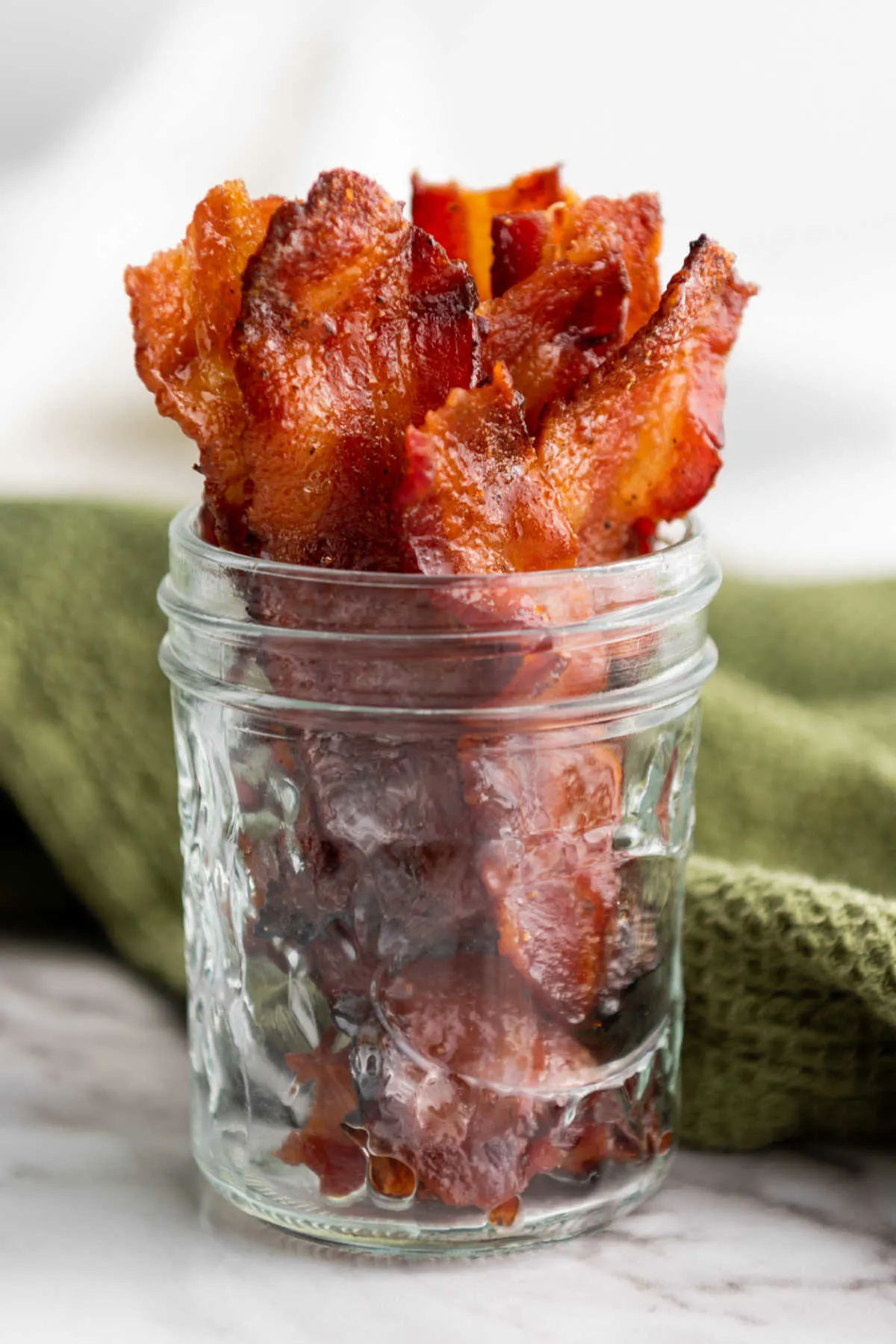 Jar with strips of maple brown sugar bacon inside showing crispy bacon with a bit of a shiny glaze.