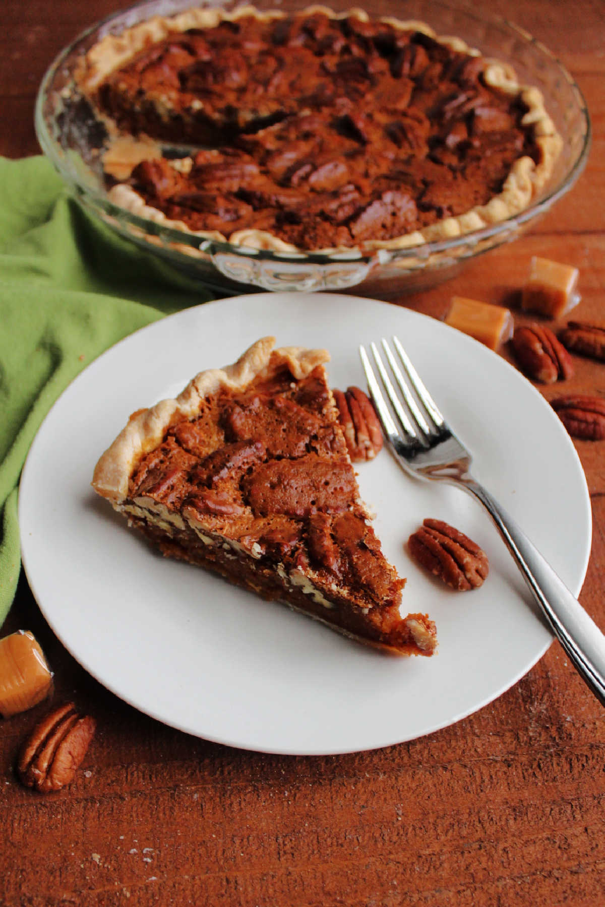 Slice of caramel pecan pie served with remaining pie in the background.
