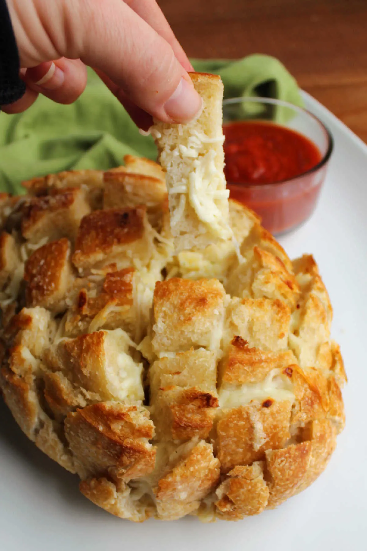 Pulling a piece of cheesy garlic bread out of a loaf of sourdough bread.