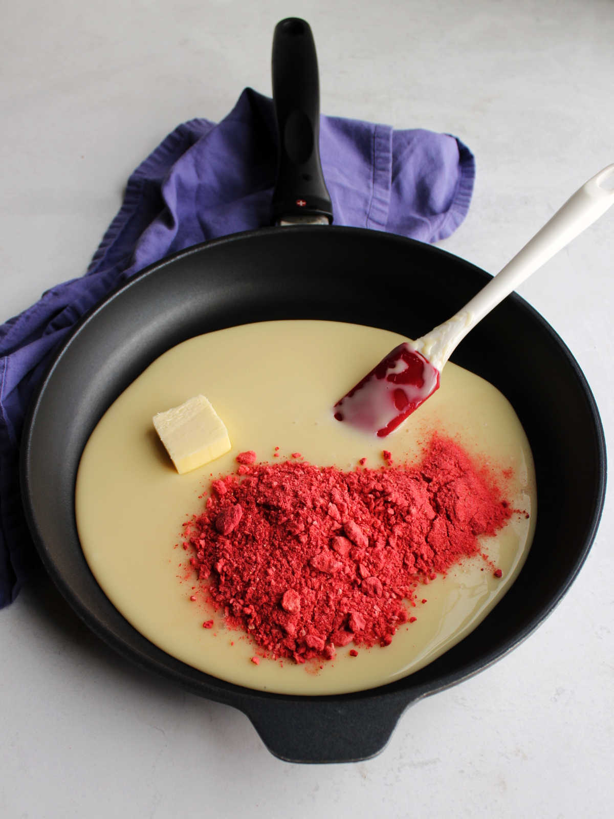 Skillet with condensed milk, butter and crushed freeze-dried strawberries inside ready to cook.
