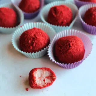 Strawberry brigadeiro with a bite missing showing creamy pink interior and red freeze-dried strawberry powder on the outside.