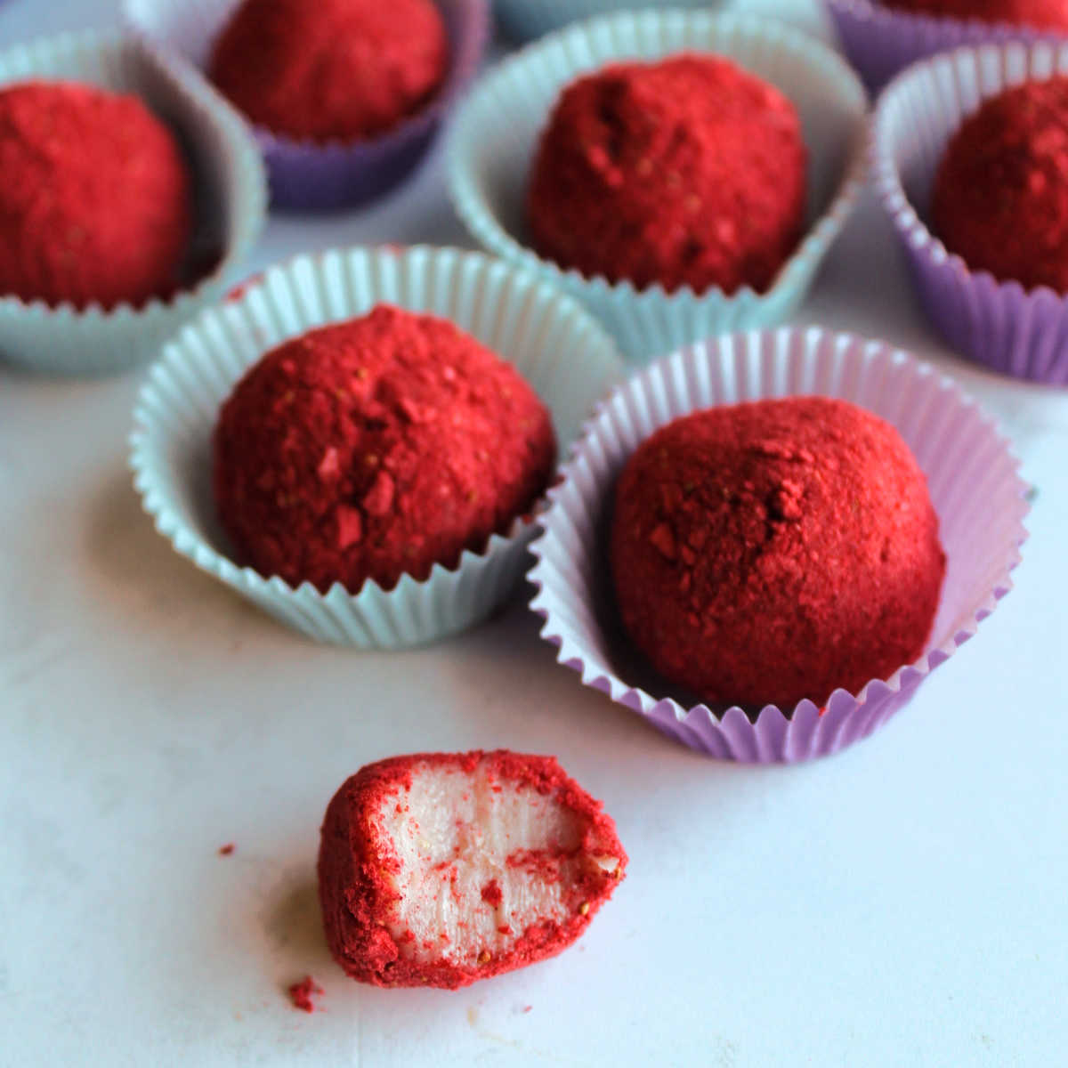 Strawberry brigadeiro with a bite missing showing creamy pink interior and red freeze-dried strawberry powder on the outside.