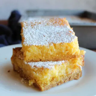 Stack of lemon gooey butter cake bars with cakey crust and gooey cream cheese, lemon and butter topping.