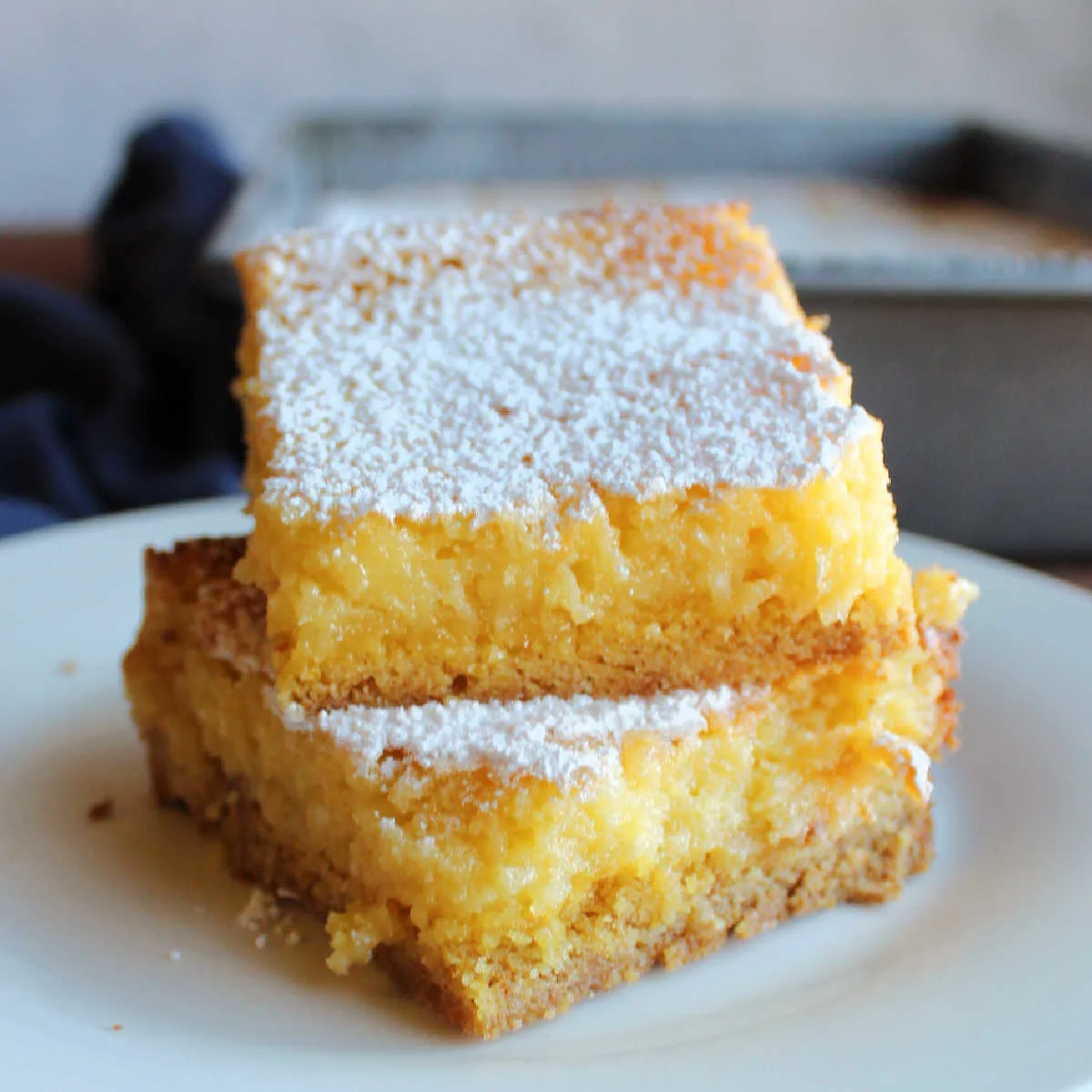 Stack of lemon gooey butter cake bars with cakey crust and gooey cream cheese, lemon and butter topping.