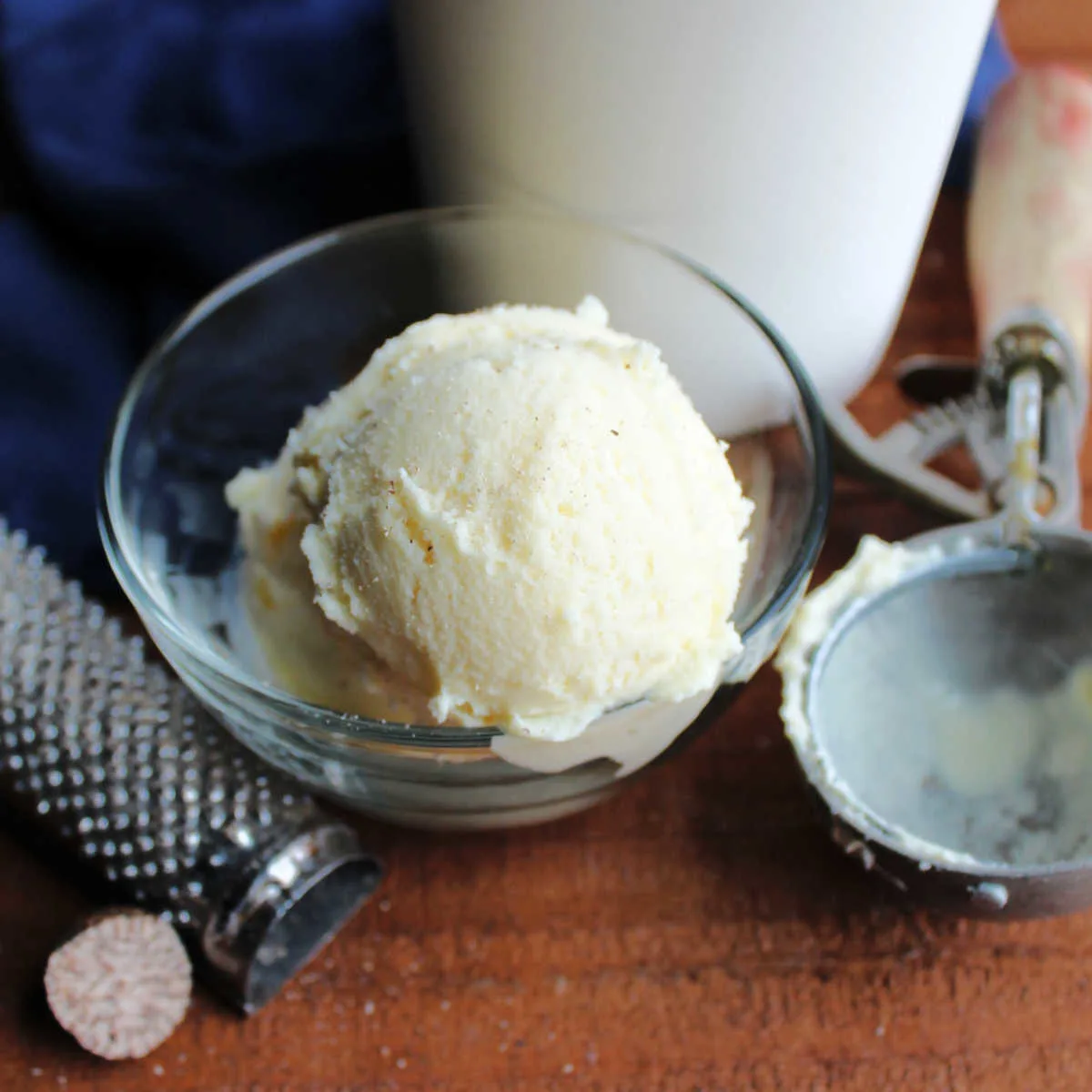 Scoop of eggnog ice cream next to nutmeg grater and an antique scoop.