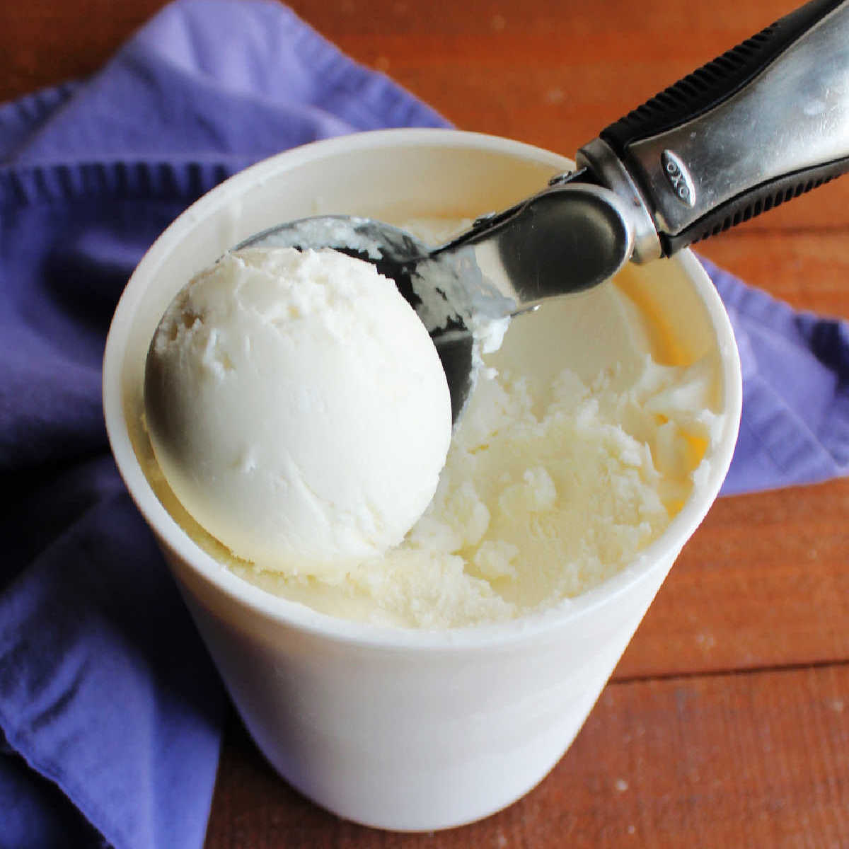Scooping out vanilla frozen yogurt from a freezer container.