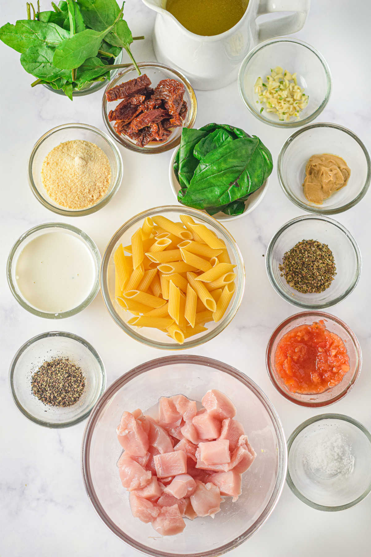 Ingredients including chicken, pasta, spinach, cheese, sun dried tomatoes, chream and spices ready to be made into creamy tuscan chicken pasta.