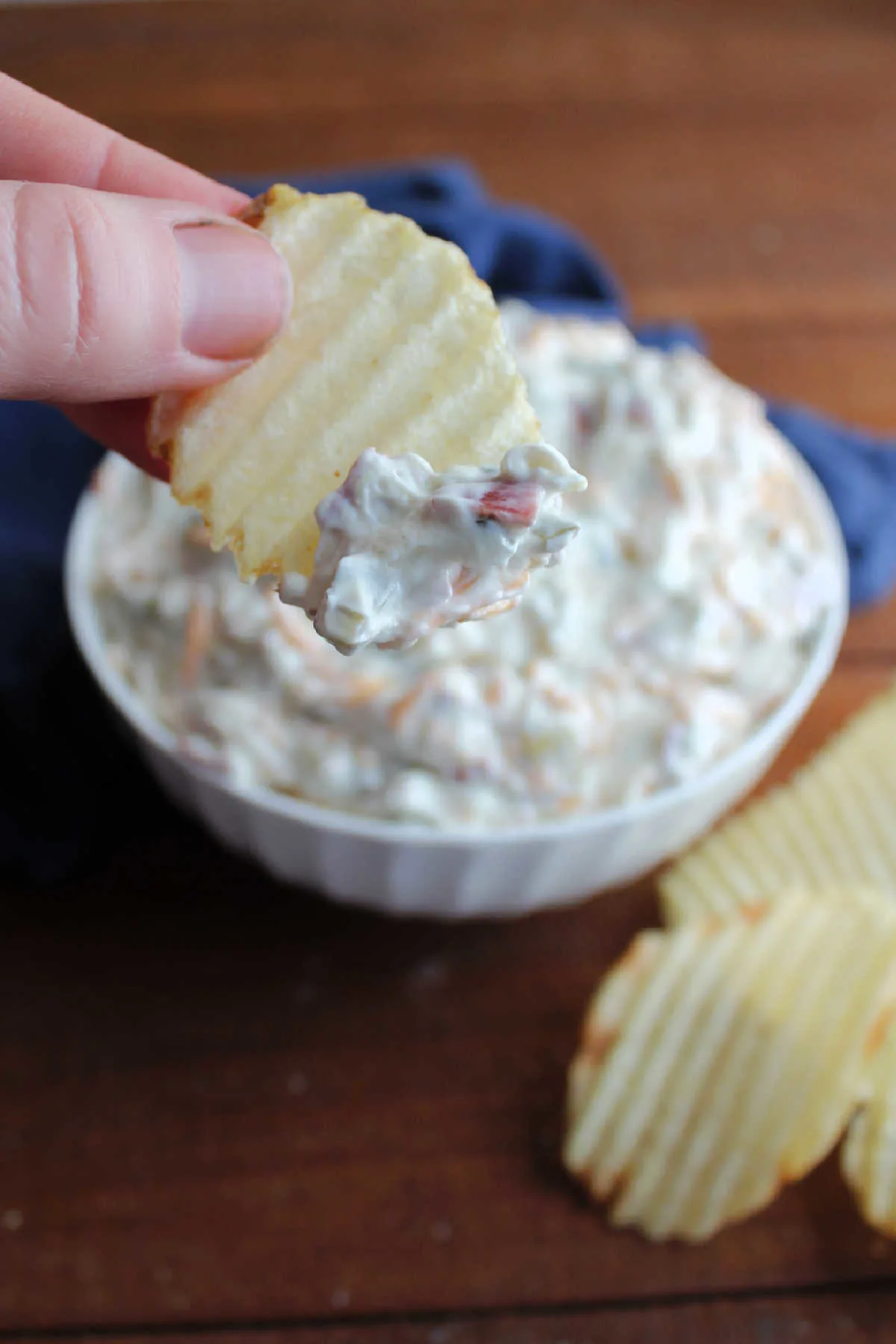 Dipping a ruffled potato chip into a bowl of dill pickle wrap dip. 