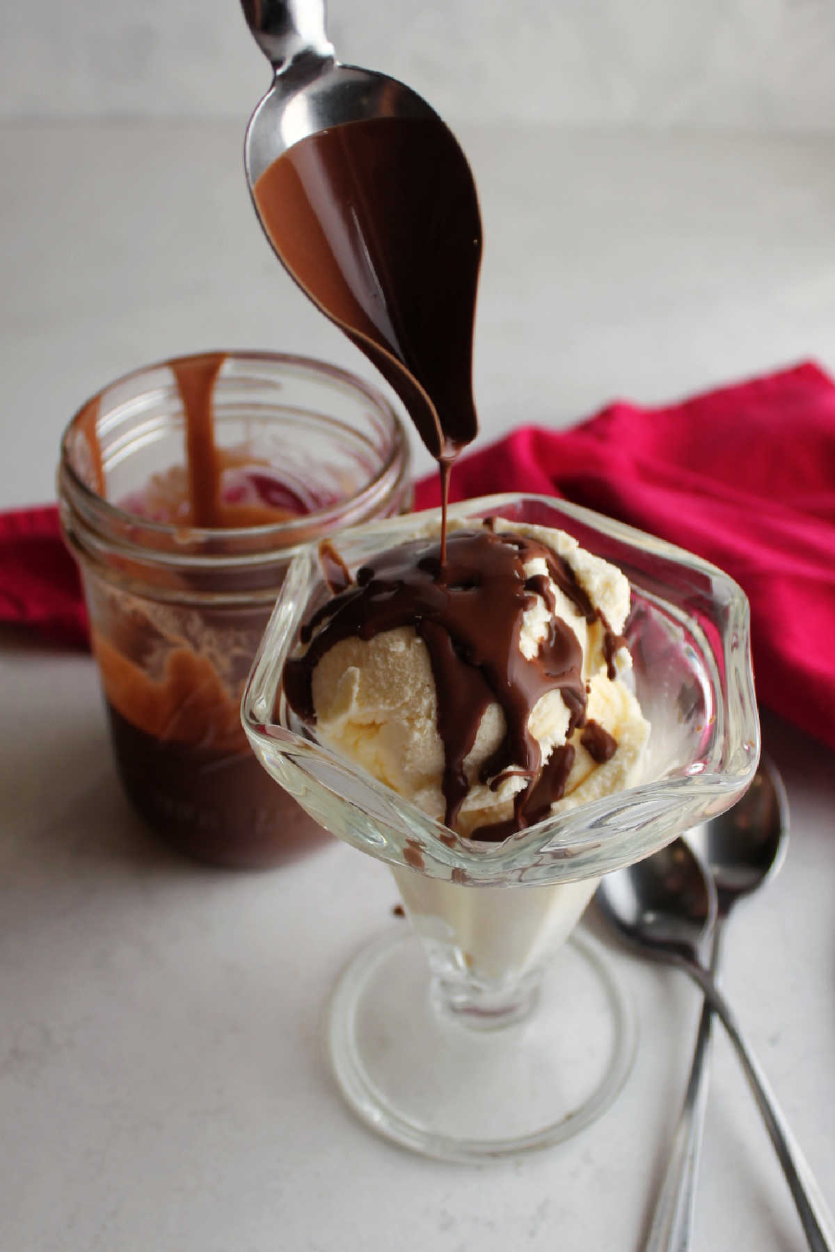 Spoon drizzling warm chocolate magic shell over bowl of vanilla ice cream. 