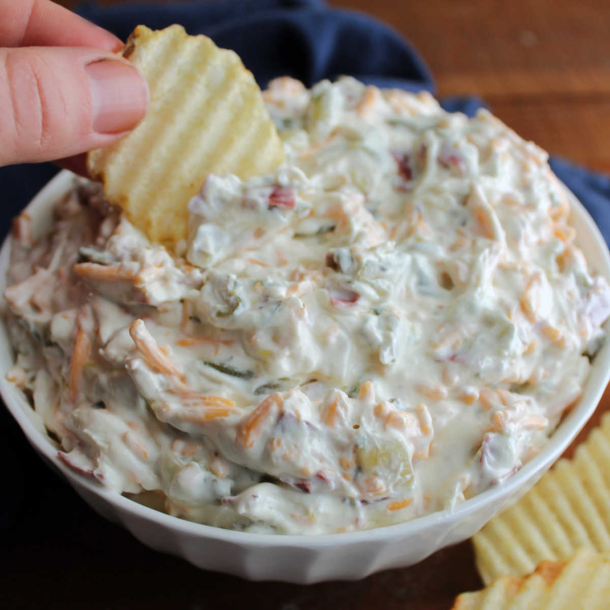 Dipping ruffled chip into dill pickle dip with shredded cheddar cheese and dried beef inside.