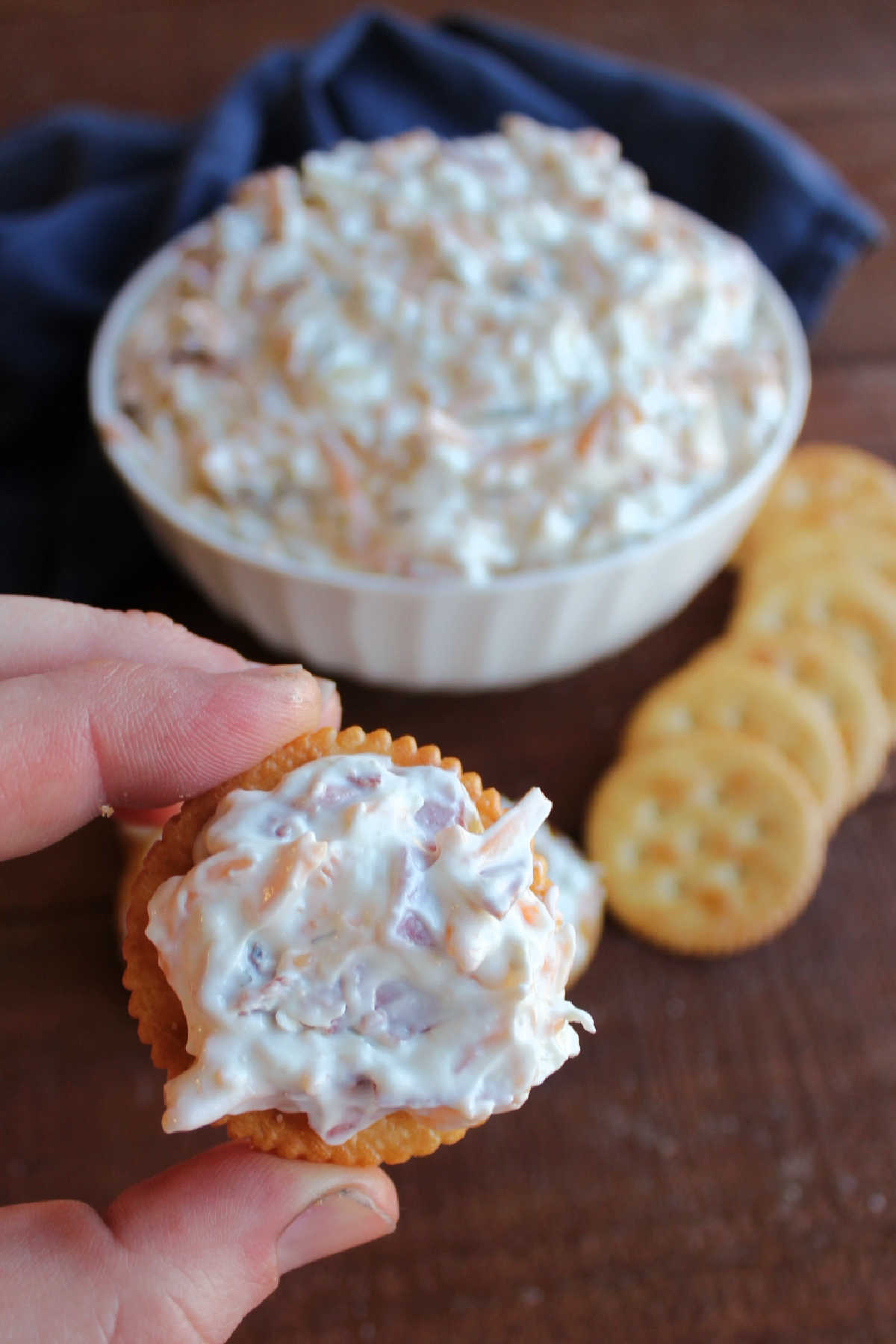 Hand holding Ritz cracker with dill pickle dip spread over the top.