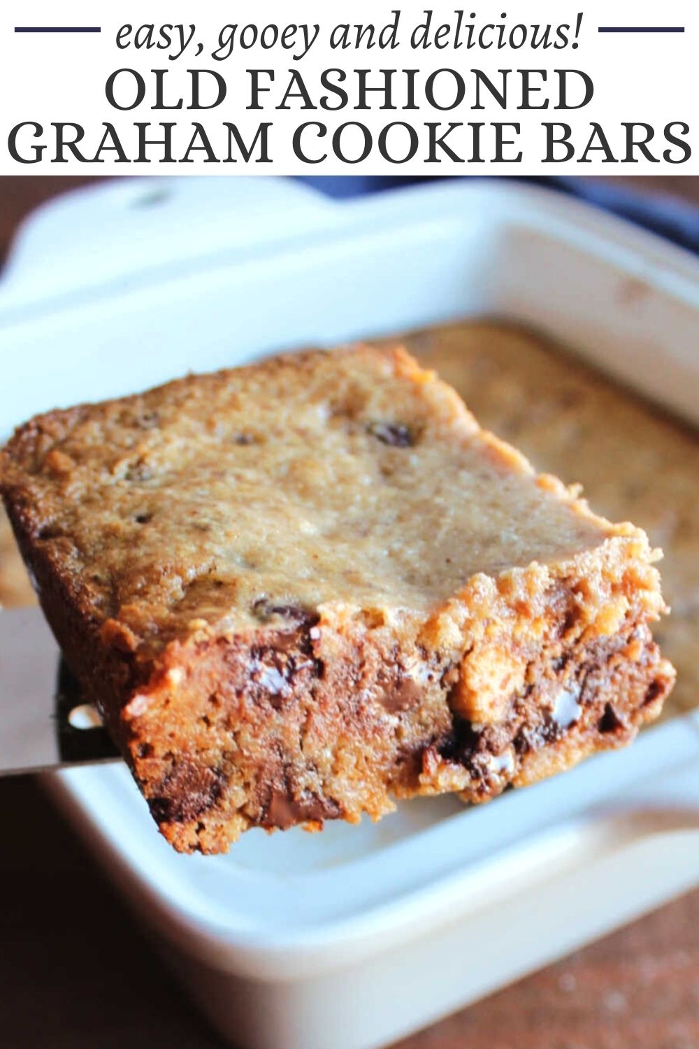 This is a photo of a Graham Cookie Bar on a small spatula, being served from a white square baking pan baked with the bars.