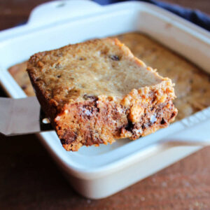 Lifting square of gooey graham cookie bar out of pan showing crispy edge and gooey center.