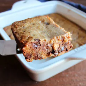 Lifting square of gooey graham cookie bar out of pan showing crispy edge and gooey center.