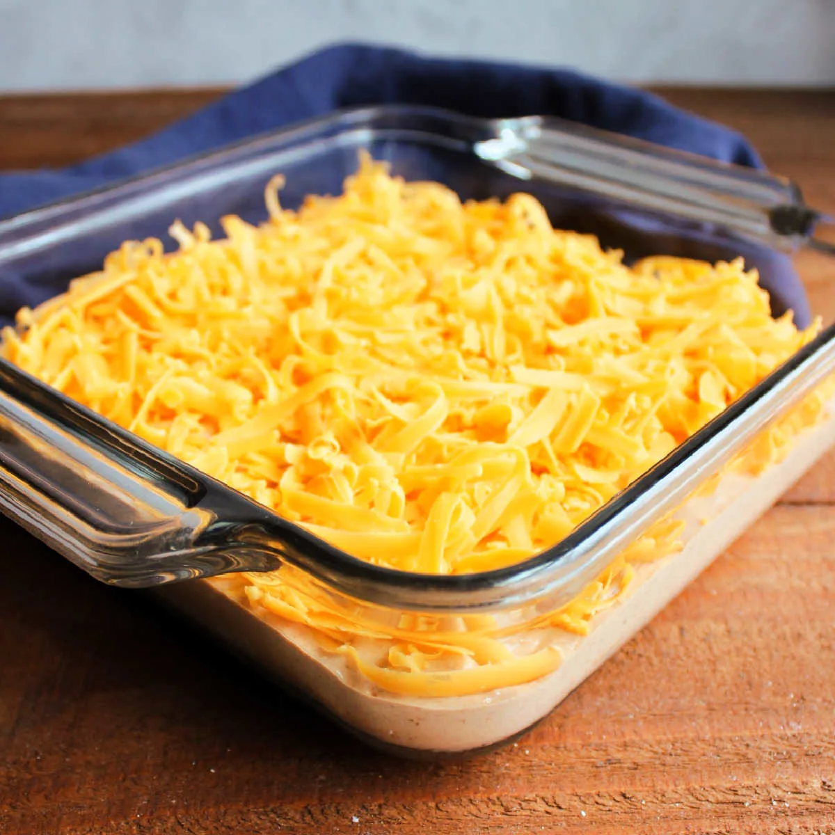 Bean mixture in glass baking dish, topped with freshly shredded cheddar cheese, ready to go in the oven.