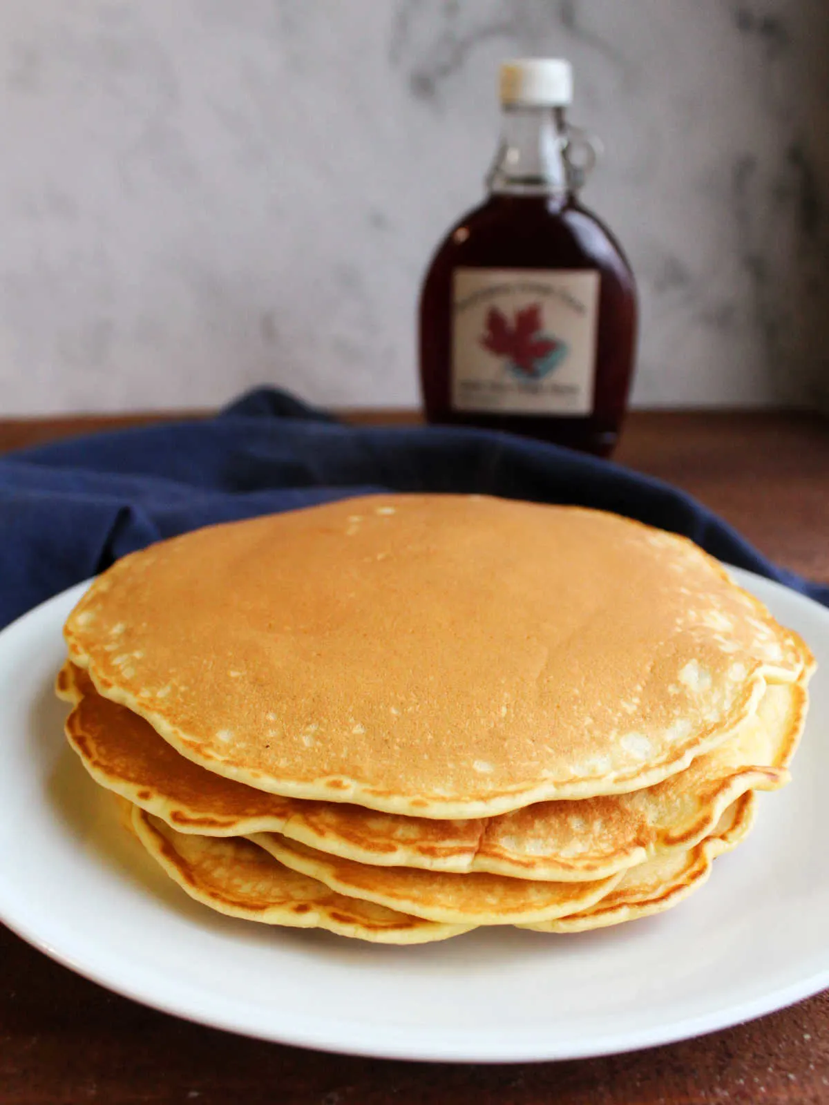Stack of golden brown pancakes on plate in front of bottle of pure maple syrup.