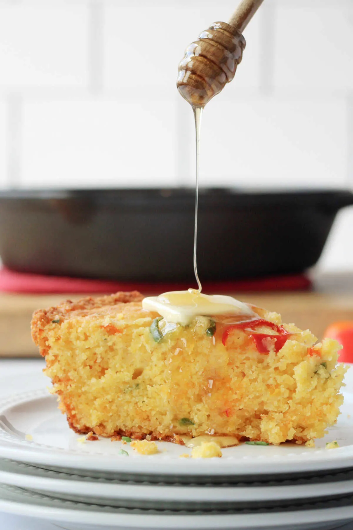 Honey being drizzled over slice of loaded cornbread topped with a pat of butter.