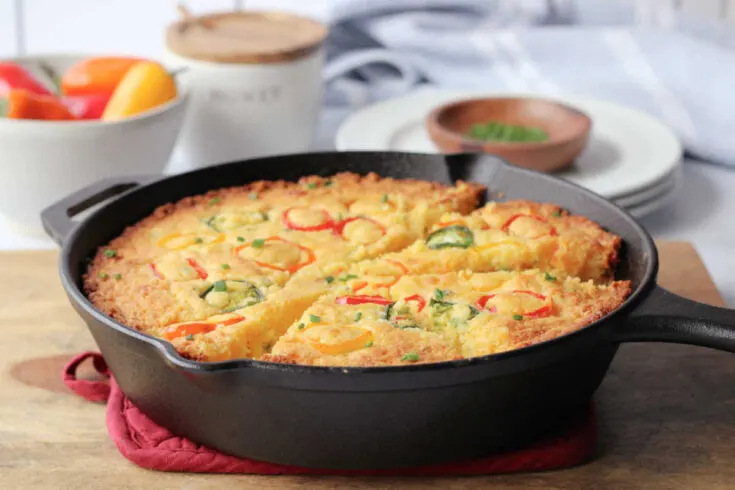 Skillet filled with loaded cornbread with rings of jalapeno and sweet peppers baked on the top.
