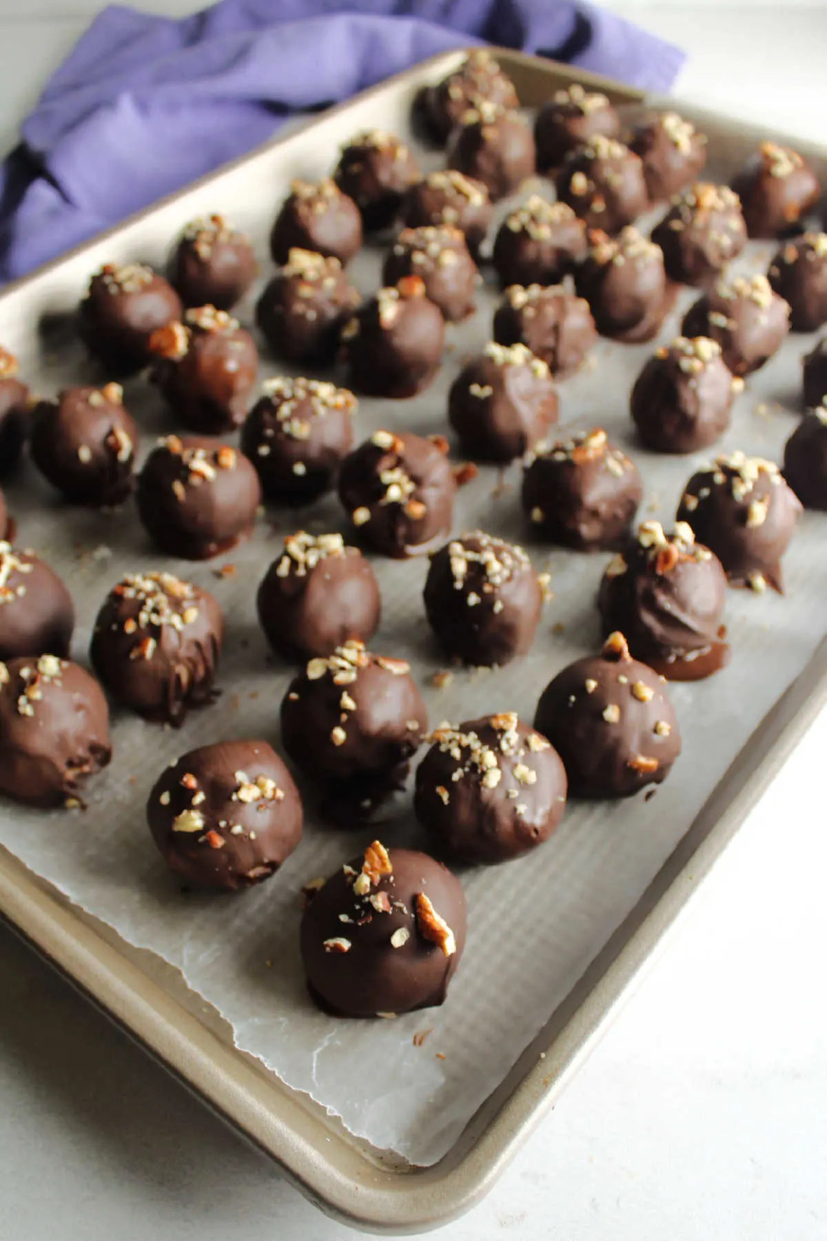 Chocolate coated coconut bon bons topped with bits of chopped pecans, setting up on wax paper lined tray.