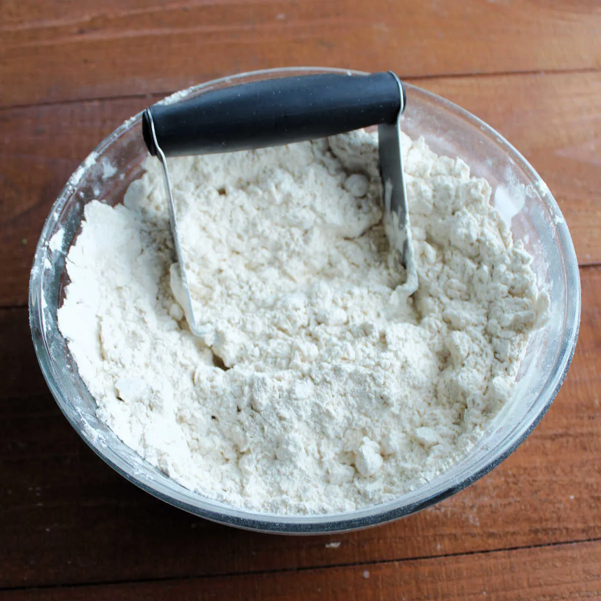 Mixing bowl of flour with lard cut into it with a pastry cutter, showing crumbly texture.
