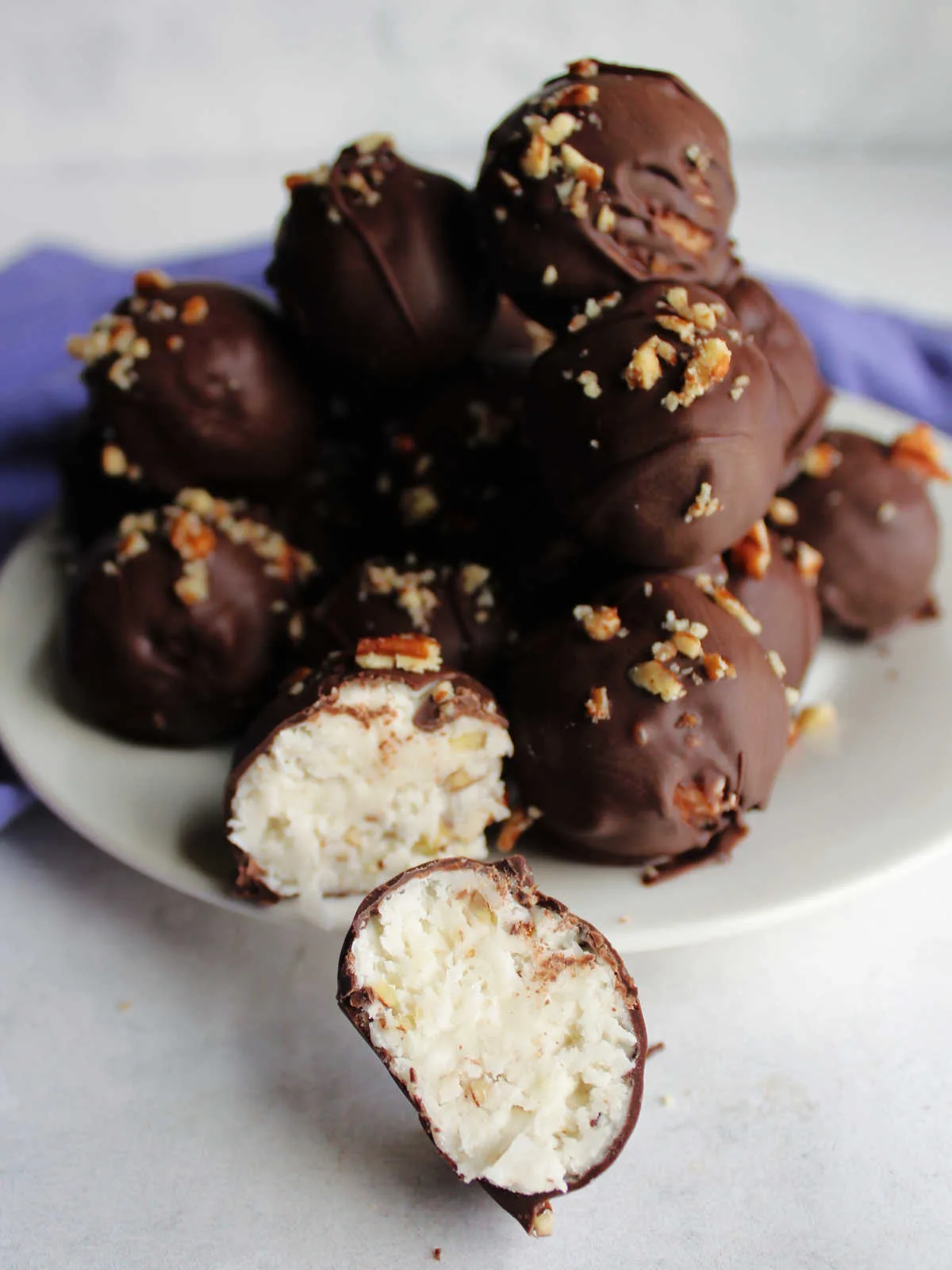 Pile of coconut bon bons topped with pecans in background with a bon bon cut in half in the front, showing the white filling.