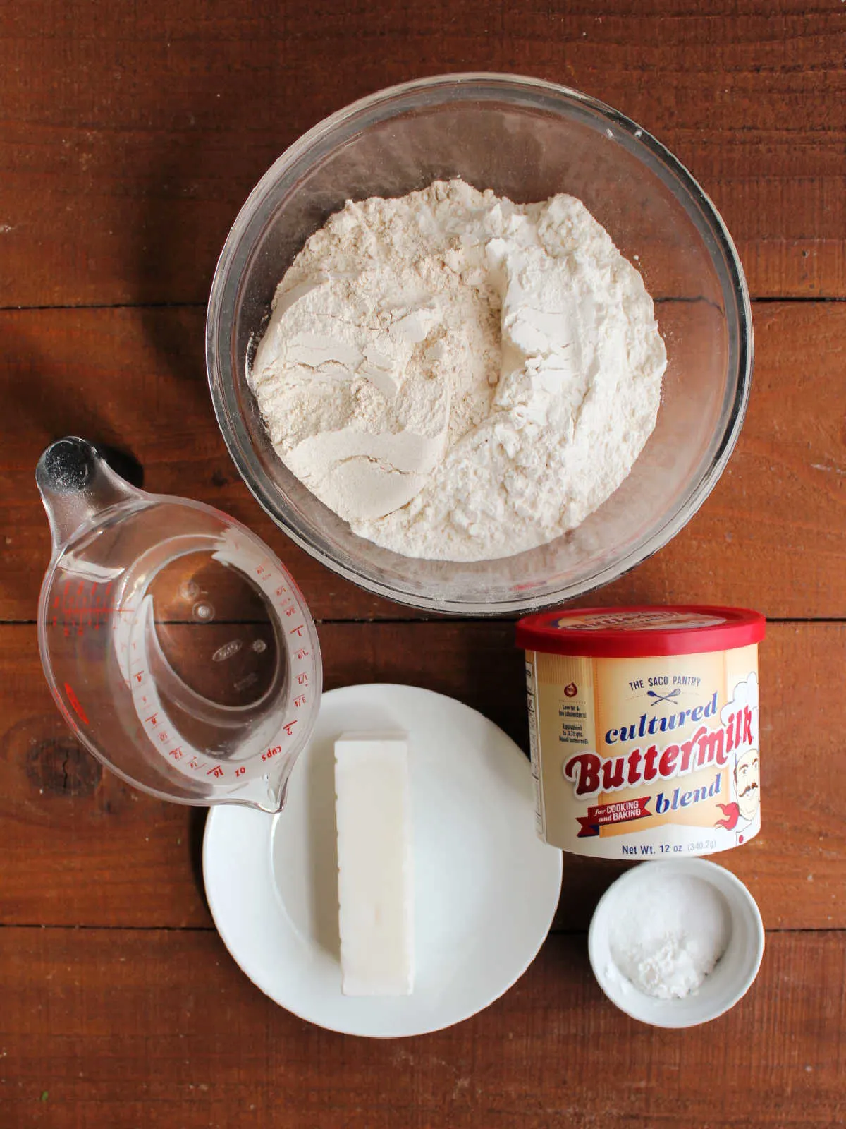 Ingredients including flour, buttermilk powder, baking powder, baking soda, salt, lard and cold water ready to be made into biscuits.