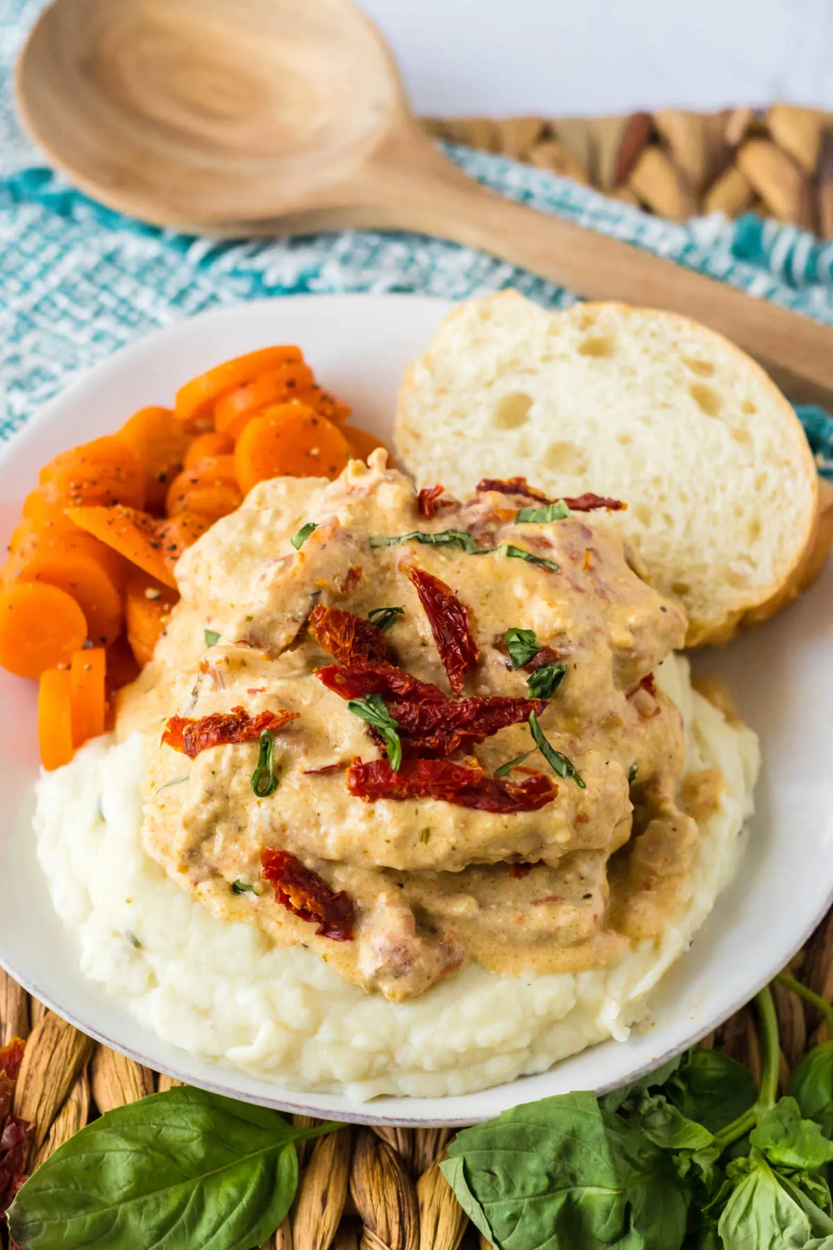 Dinner plate of slow cooker marry me pork chops garnished with extra sun dried tomatoes and basil served with mashed potatoes and carrots.