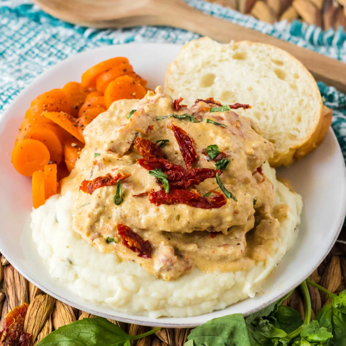 Dinner plate featuring sun dried tomato topped marry me pork chops on a bed of mashed potatoes served with carrots and bread.