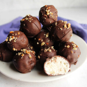 Plate of chocolate dipped coconut bon bons with one cut in half showing creamy center.